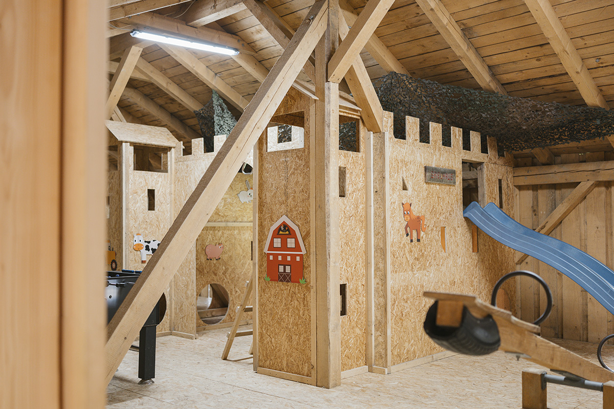 Schaukel, Holzburg, Rutsche und Kickerkasten in unserem Indoor-Spielplatz