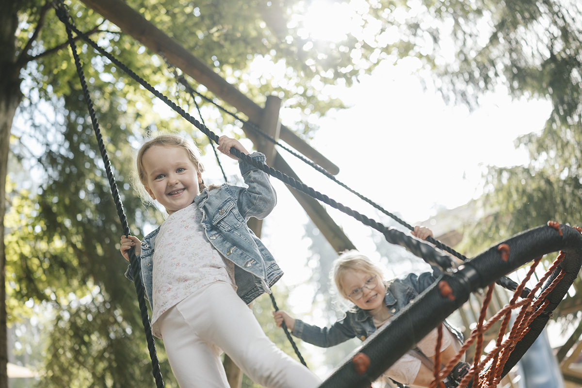 Spielende Mädchen in einer Nestschaukel auf dem Spielplatz des Hofs
