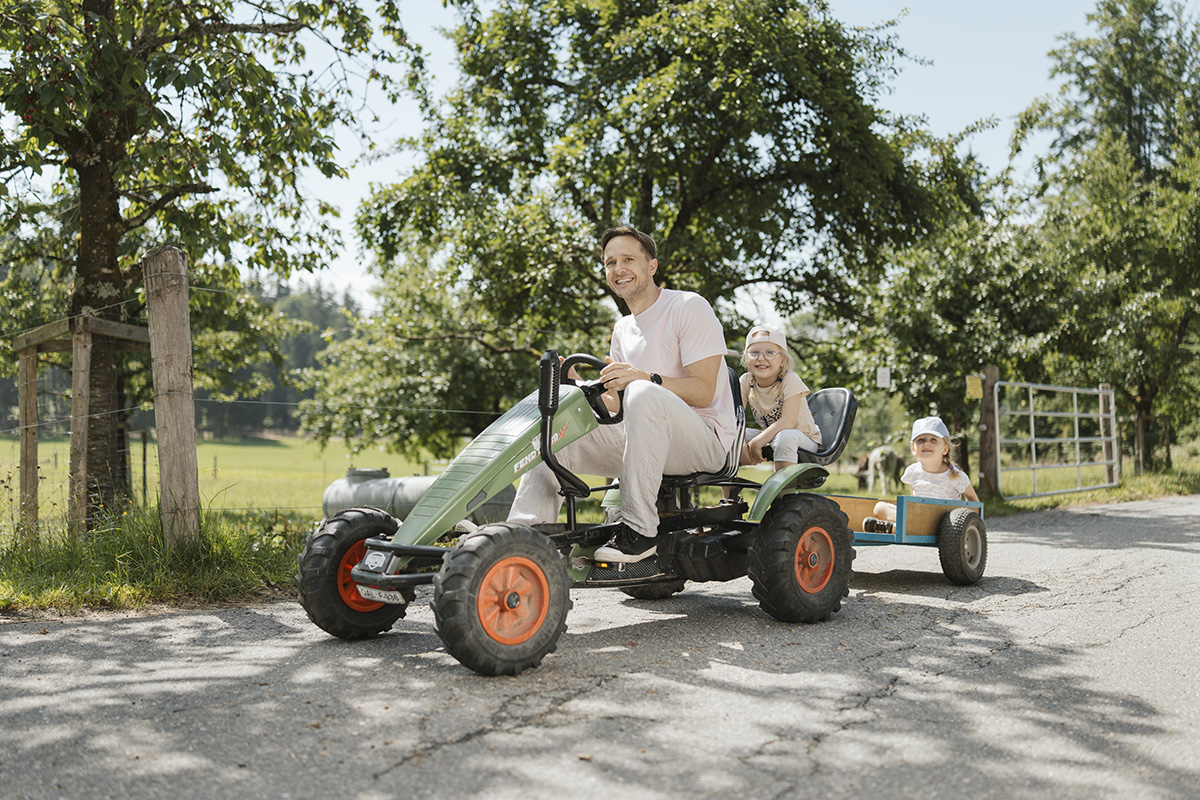 Vater fährt mit seinen zwei Kindern mit einem kleinen Tret-Bulldog mit Anhänger